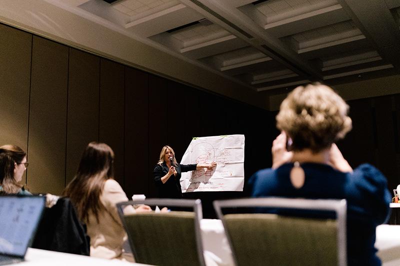 A conference presenter points to a diagram on a large piece of paper