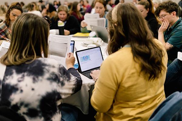 A person types on a laptop while sitting at a table at a conference.