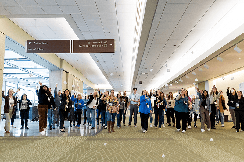 A group of conference attendees throw pieces of paper in the air as part of a conference workshop