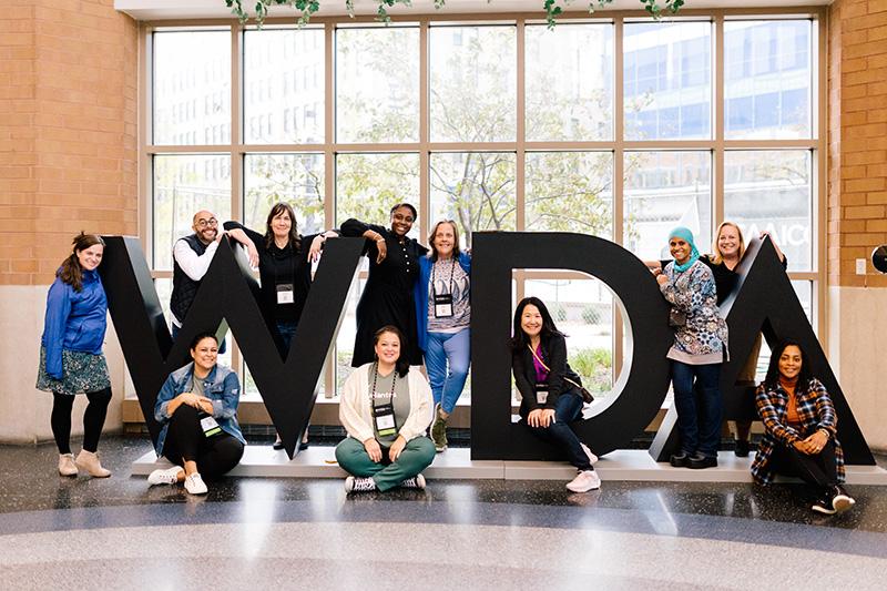 Group of conference attendees standing around a large 3D sign spelling out WIDA