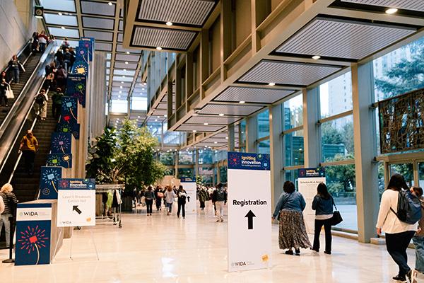 Conference attendees walk through a convention center lobby with a sign pointing to registration.